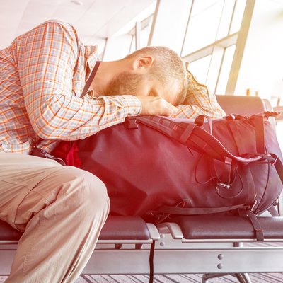 Erschöpfter Fluggast schläft auf Reisetasche in Wartehalle