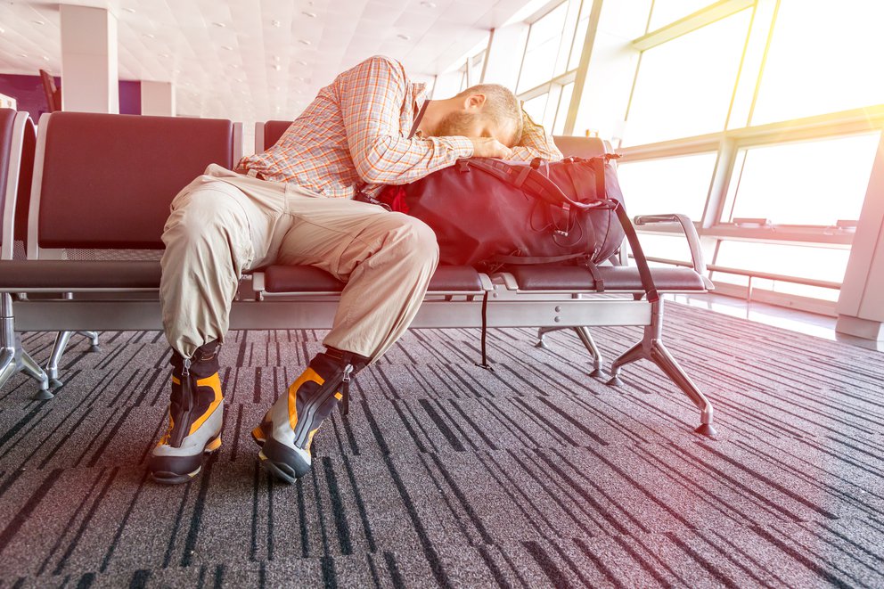 Erschöpfter Fluggast schläft auf Reisetasche in Wartehalle