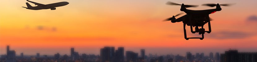 Drohnen-Silhouette vor Skyline einer Stadt im Sonnenuntergang
