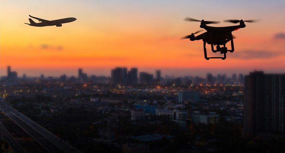 Drohnen-Silhouette vor Skyline einer Stadt im Sonnenuntergang