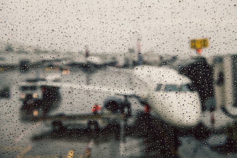 Fenster mit Regentropfen, dahinter Flugzeug während des Boardings