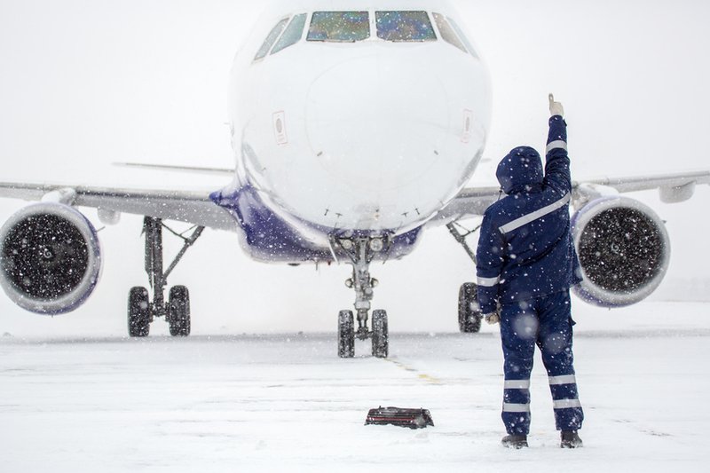 Fluglotse im Schnee vor Flugzeug auf verschneitem Rollfeld