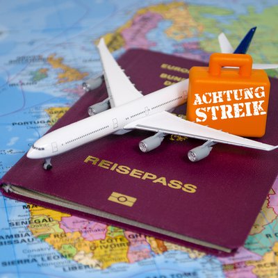 Reisepass und Miniatur-Flugzeug mit "Achtung Streik"-Schild liegen auf einer Landkarte