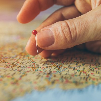 Eine Hand mit einer Stecknadel über einer Landkarte